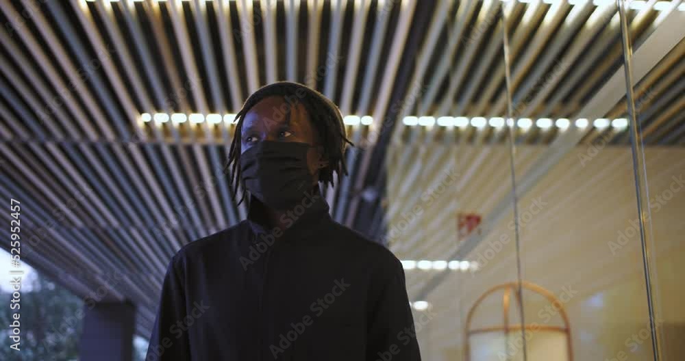 Portrait young black man wearing wearing a medical coronavirus protective mask and standing outside in street looking at camera. African American person portrait. High quality 4k footage Portrait young black man wearing wearing a medical coronavirus protective mask and standing outside in street looking at camera. African American person portrait. High quality 4k footage