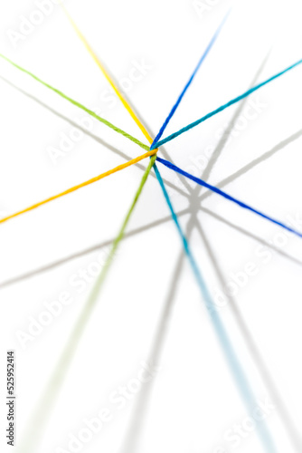 Yellow, green, blue, teal, yarn intertwined and radiating outward casting shadows on a white background.