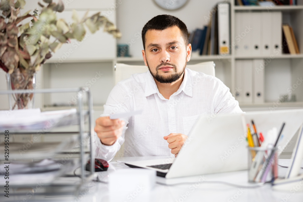 Portrait of man office worker sitting at table, looking at camera and giving document.