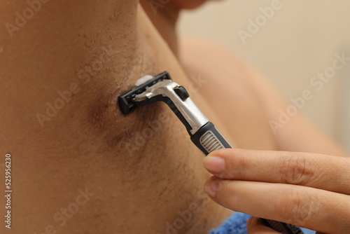 Female unshaved armpits or woman with long hair underarm, depilation, hair removal concept. Young woman shaves hairy armpits with a disposable razor. Close-up, selective focus.