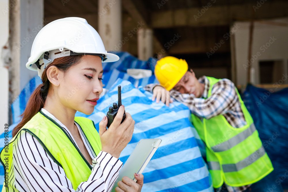 An engineer woman holding a radio to report the work of a construction worker sleeping on the job site. Industrial concept of building construction projects. Labor welfare. labor insurance An engineer woman holding a radio to report the work of a construction worker sleeping on the job site. Industrial concept of building construction projects. Labor welfare. labor insurance
