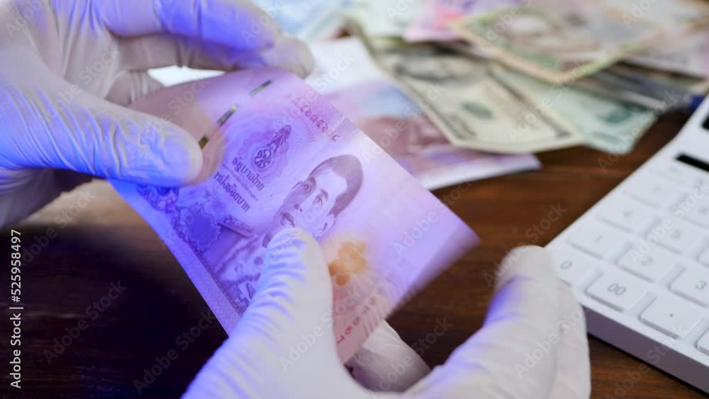 Inspection of detail and lit up security strip thai baht banknote. Business or financial. Illegal counterfeit paper money. Hand in white gloves under blacklight or ultraviolet lamp. Check cash in bank Inspection of detail and lit up security strip thai baht banknote. Business or financial. Illegal counterfeit paper money. Hand in white gloves under blacklight or ultraviolet lamp. Check cash in bank