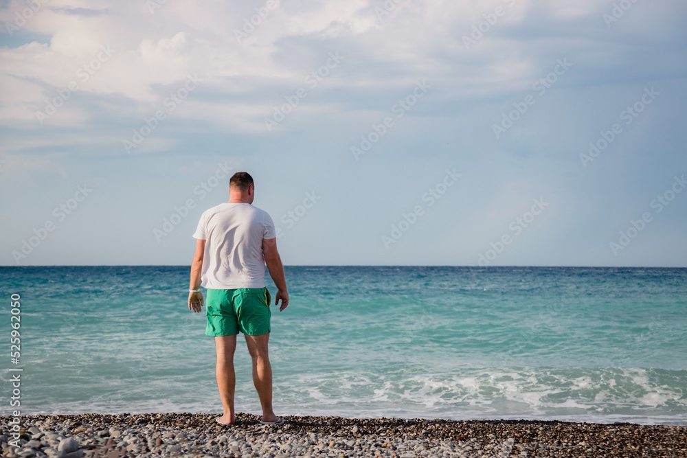 attractive young adult man stands with his back on the shore of the mediterranean sea with waves. copy space