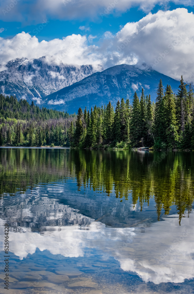Reflections on Pyramid Lake in Jasper National Park with canoes nestled in the trees in the background 
