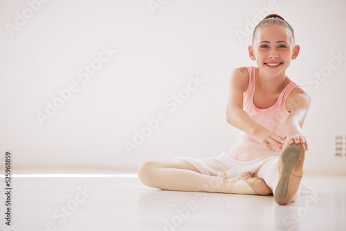Happy ballet dancer girl stretching on the floor in a dance studio with mockup white background. Portrait ballerina kid smile while learning or training with legs in class for a performance mock up