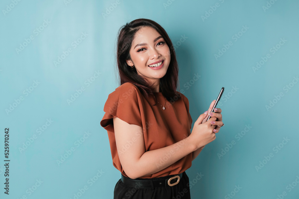 Naklejka premium A portrait of a happy Asian woman is smiling and holding his smartphone wearing brown shirt