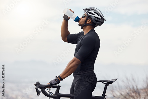 Fototapeta Sports man with a bike drinking water bottle doing fitness training or workout on sky mockup background