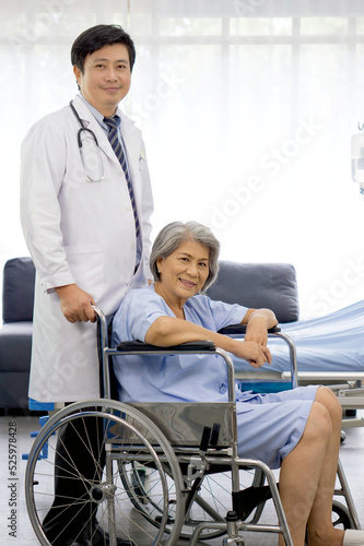 Portrait of asian doctor with stethoscope and gown push a wheelchair of the elderly patient. Healthcare and medicine concept.