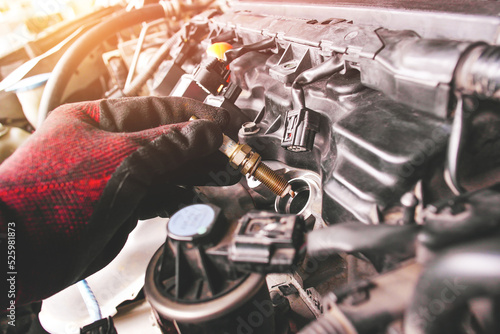 A auto mechanic is installing automobile iridium spark plugs into the ignition socket of the engine block in the engine compartment. photo