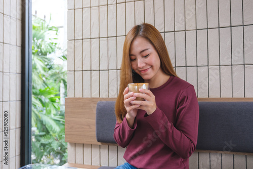 Portrait image of a beautiful young woman holding and drinking hot coffee in cafe