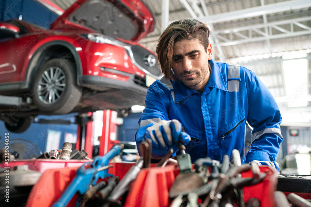Male car operator wearing blue overalls, gloves working under the hood of car and checking attentively serviceability of engine at repair garage. Concept of car maintenance Male car operator wearing blue overalls, gloves working under the hood of car and checking attentively serviceability of engine at repair garage. Concept of car maintenance