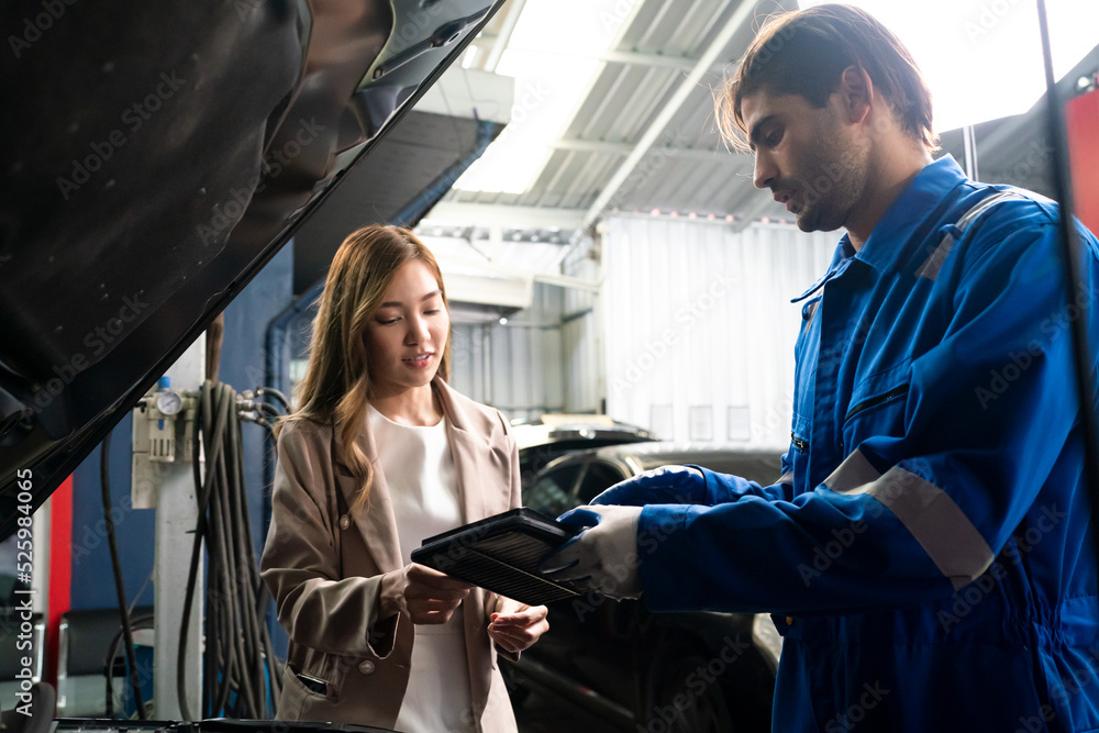 Male car operator wearing blue overalls, gloves working under the hood of car and checking attentively serviceability of engine at repair garage. Concept of car maintenance Male car operator wearing blue overalls, gloves working under the hood of car and checking attentively serviceability of engine at repair garage. Concept of car maintenance