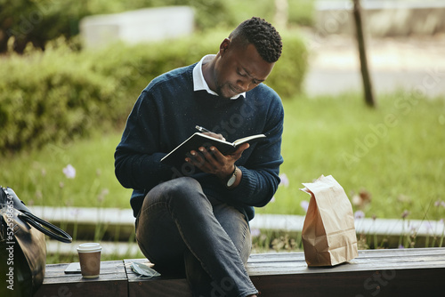 Writing, creative thinking and planning businessman sitting on park bench working on corporate strategy. Employee man taking lunch break from office to work on schedule and write in a notebook. photo