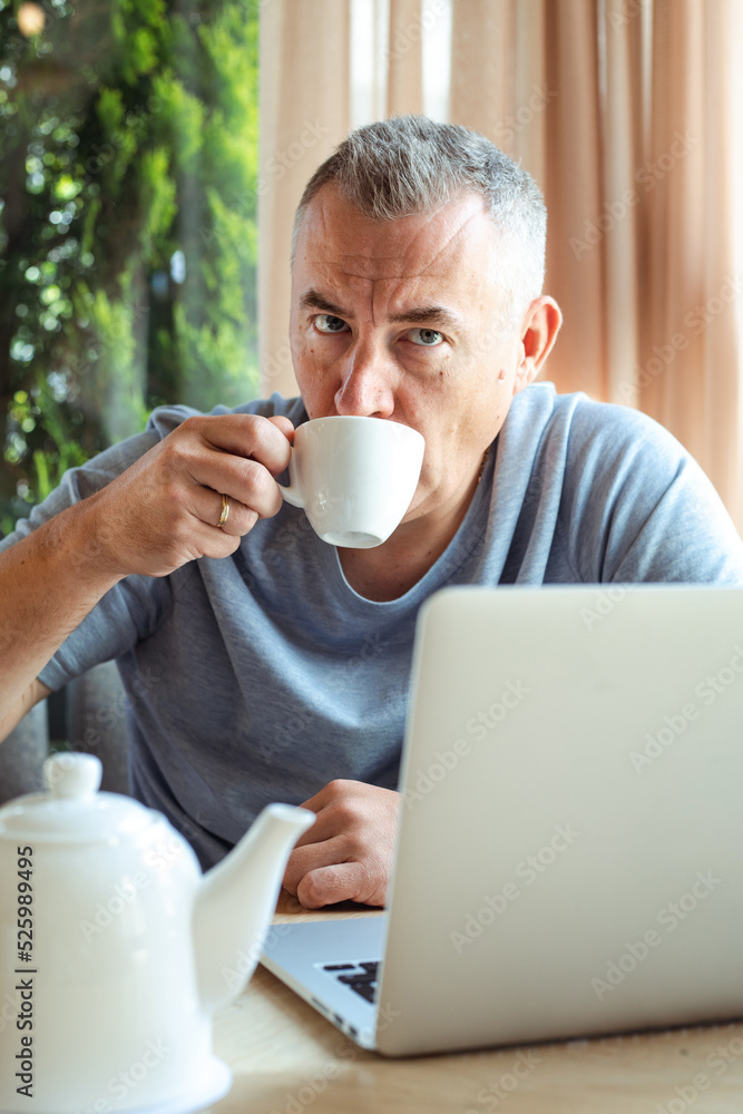 Aged attractive business man sitting in cozy cafe, drink tea and working on laptop. Implementation of modern technologies into urban lifestyle. Remote job, working time, freelance, busy people Aged attractive business man sitting in cozy cafe, drink tea and working on laptop. Implementation of modern technologies into urban lifestyle. Remote job, working time, freelance, busy people