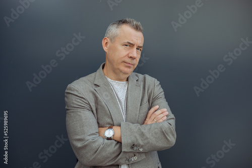 Bilde på lerret Portrait of successful aged gray haired businessman standing with crossed arms in stylish suit and luxury watch on gray background