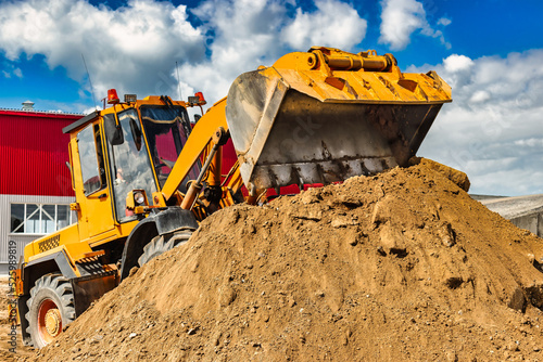 A large front loader pours sand into a pile at a construction site. Transportation of bulk materials. Construction equipment. Bulk cargo transportation. Excavation.