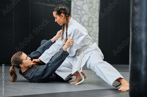Mma, karate and jiu jitsu with two female athletes practicing, training and sparring in fight class. Healthy, fit and active women in gi or uniform learning self defense for safety and health photo