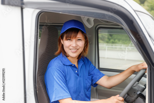 青い帽子とポロシャツを着て運転する女性。引越し、配送ドライバーのイメージ。