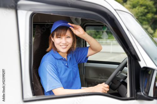 女性ドライバーが笑顔で荷物届ける。物流、宅配、引越し業者のイメージ。