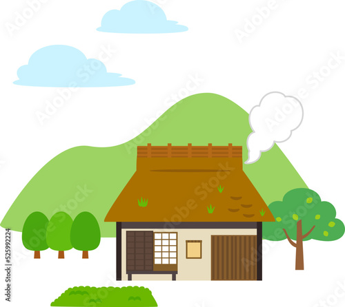 排煙している茅葺屋根の家と山の風景