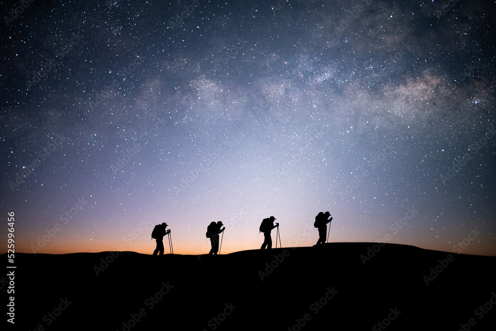 Silhouette of four young traveler and backpacker hiking to the top of the mountain with beautiful view star, milky way over the sky. He enjoyed traveling and was successful when he reached the summit.