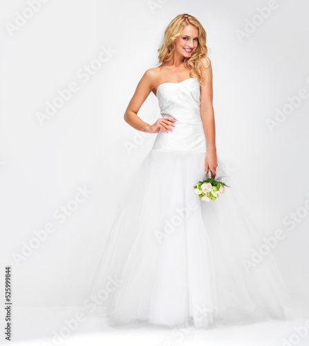 Happy woman with trendy hair, makeup and bouquet of flowers standing in studio with copy space. Portrait of a beautiful, marriage and bride model in an elegant wedding dress with a white background.