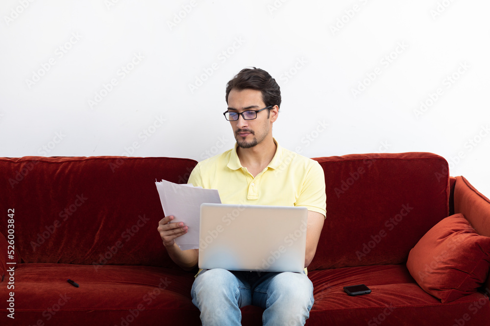 Handsome man sitting on the couch and working on laptop at home. Online education and distant work concept