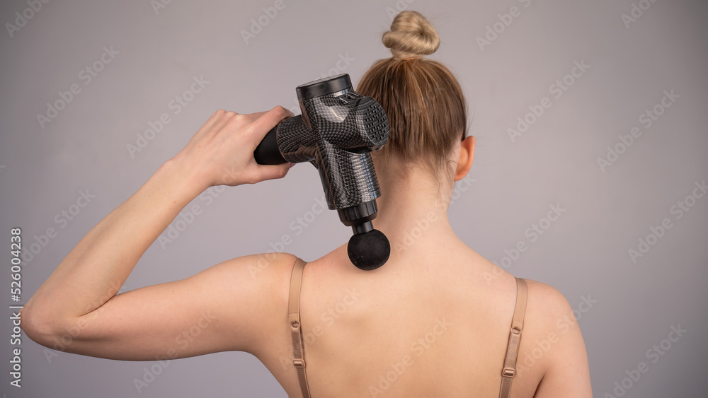Caucasian woman giving herself a back massage with a gun. Caucasian woman giving herself a back massage with a gun.