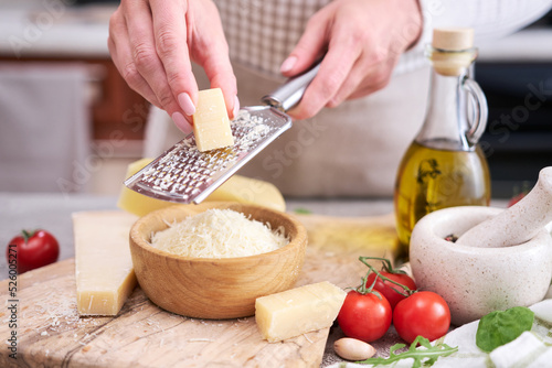 Woman grates Parmesan cheese on a wooden cutting board at domestic kitchen