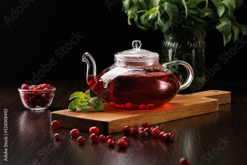 Red herbal tea with cranberries and mint in a glass teapot on a black background. A bunch of mint in the background. Selective focus, side view.