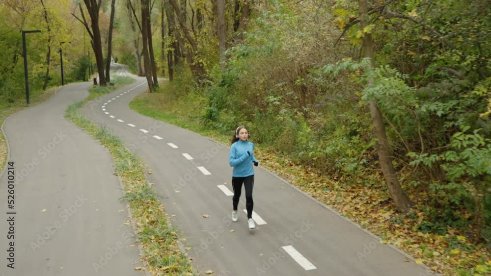 Slow motion fit female jogger running in park in the morning, autumn leaves lying on ground, male jogger running in the opposite direction, tracking shot from above. Healthy lifestyle Slow motion fit female jogger running in park in the morning, autumn leaves lying on ground, male jogger running in the opposite direction, tracking shot from above. Healthy lifestyle