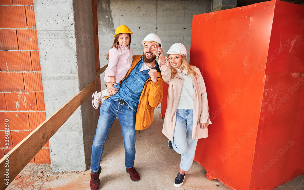Man holding daughter and smiling. Happy couple real estate house buyers demonstrating keys from new home under construction. Family life and new home purchase concept. Man holding daughter and smiling. Happy couple real estate house buyers demonstrating keys from new home under construction. Family life and new home purchase concept.