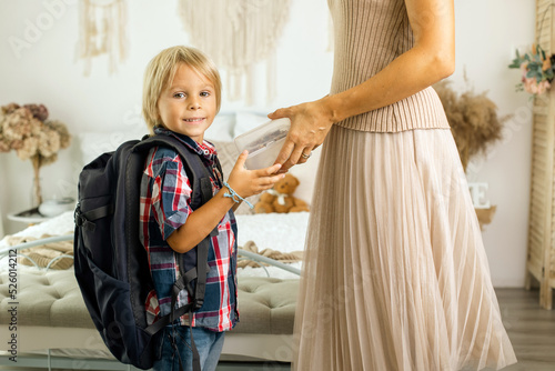 Mother, sending her firstgrader boy to school, first day at school, giving him books and a box with snack photo