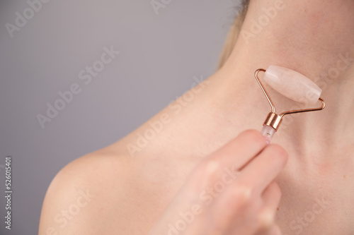 Close-up portrait of a woman using a quartz roller massager for an alternative fight against wrinkles on her neck. Smoothing of the rings of venus. 