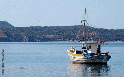 A traditional Greek fishing boat "kaiki" lays in the calm sea under a clear blue sky.