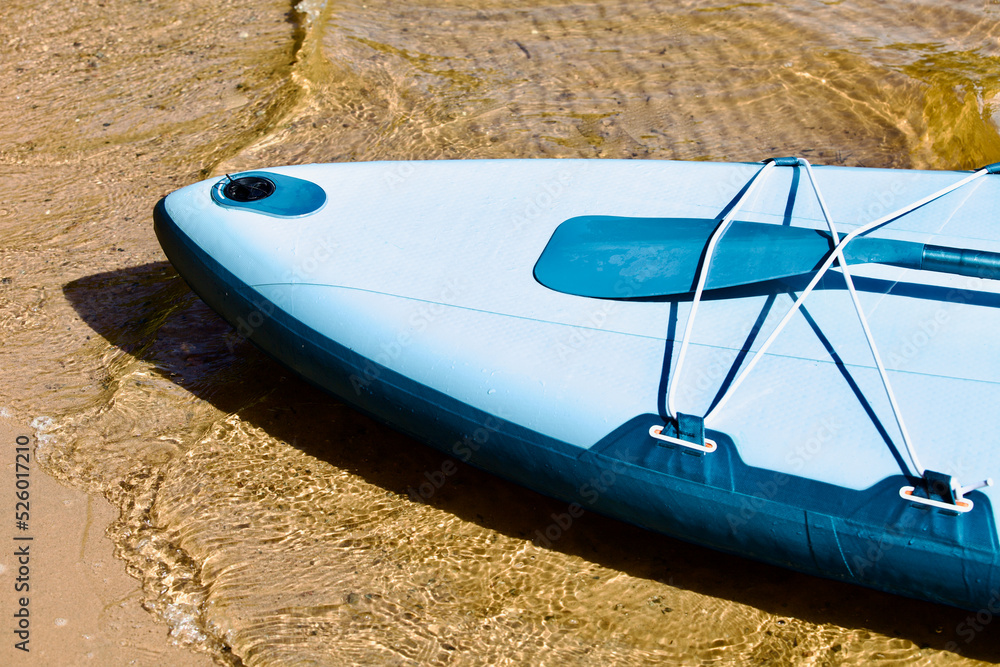 Drifting SUP board and surf board with paddle on sandy shore close up. Surfing and SUP boarding equipment in bright sun lights close-up. Outdoor water sports. Surfing lifestyle backgrounds. Surfboard. Drifting SUP board and surf board with paddle on sandy shore close up. Surfing and SUP boarding equipment in bright sun lights close-up. Outdoor water sports. Surfing lifestyle backgrounds. Surfboard.