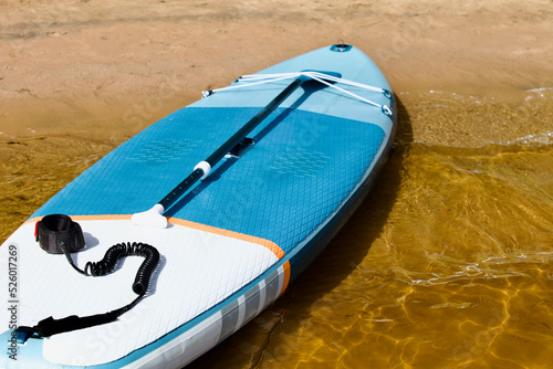 Drifting SUP board and surf board with paddle on sandy shore close up. Surfing and SUP boarding equipment in bright sun lights close-up. Outdoor water sports. Surfing lifestyle backgrounds. Surfboard.