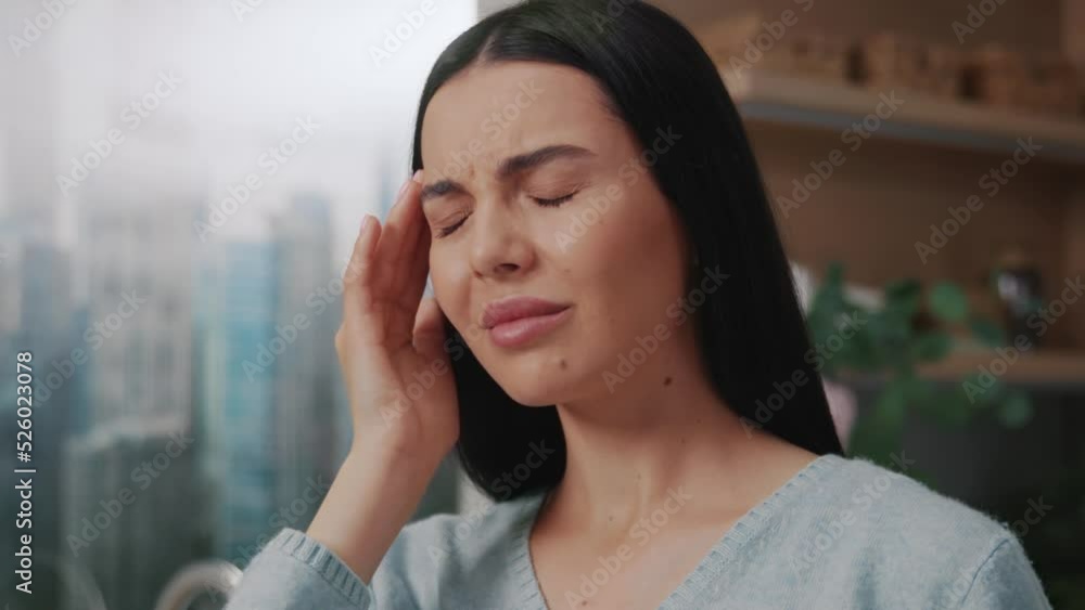 Close up woman with migraine headache standing in the kitchen. Sad touch head. Home.Stressed. Fever. Indoors Close up woman with migraine headache standing in the kitchen. Sad touch head. Home.Stressed. Fever. Indoors