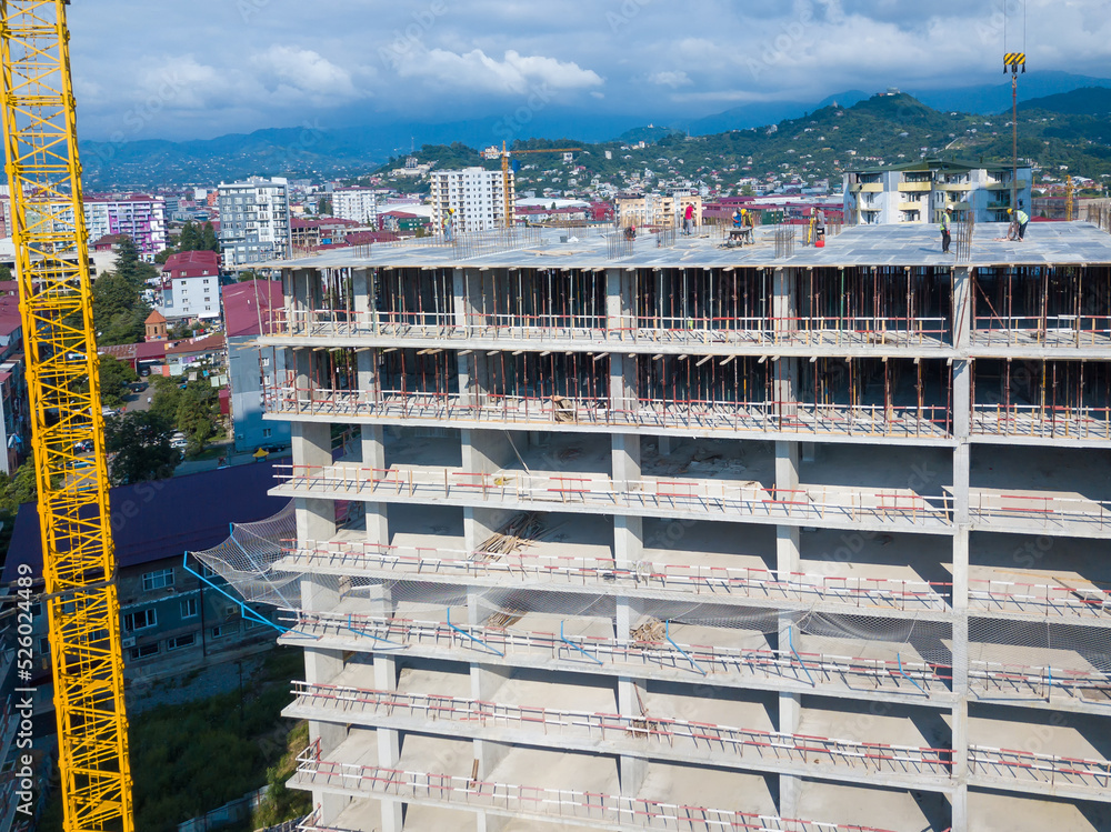 Drone view of the construction site, builders on the top floor of a building under construction against the backdrop of mountains on a sunny day Drone view of the construction site, builders on the top floor of a building under construction against the backdrop of mountains on a sunny day