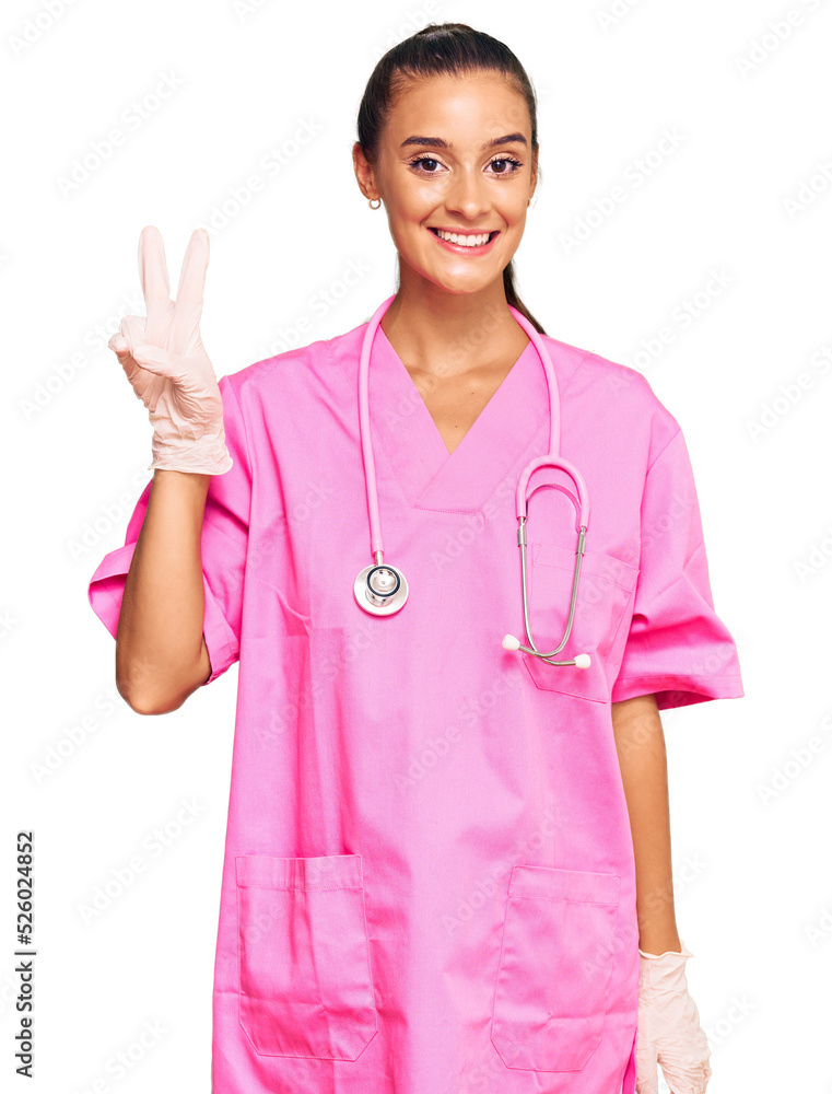 Young hispanic woman wearing doctor uniform and stethoscope smiling with happy face winking at the camera doing victory sign. number two. Young hispanic woman wearing doctor uniform and stethoscope smiling with happy face winking at the camera doing victory sign. number two.