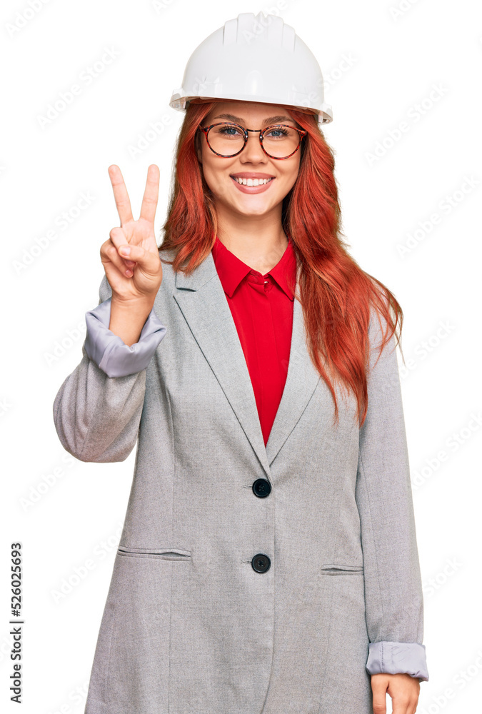 Young redhead woman wearing architect hardhat showing and pointing up with fingers number two while smiling confident and happy.