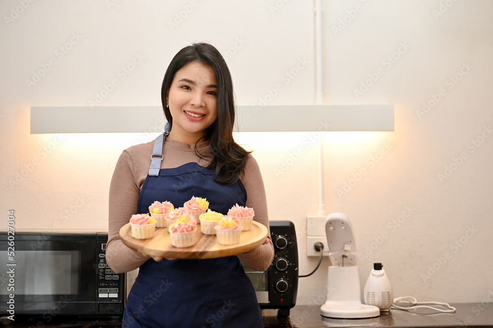 Beautiful Asian woman making cupcake and showing cupcake to the camera Beautiful Asian woman making cupcake and showing cupcake to the camera