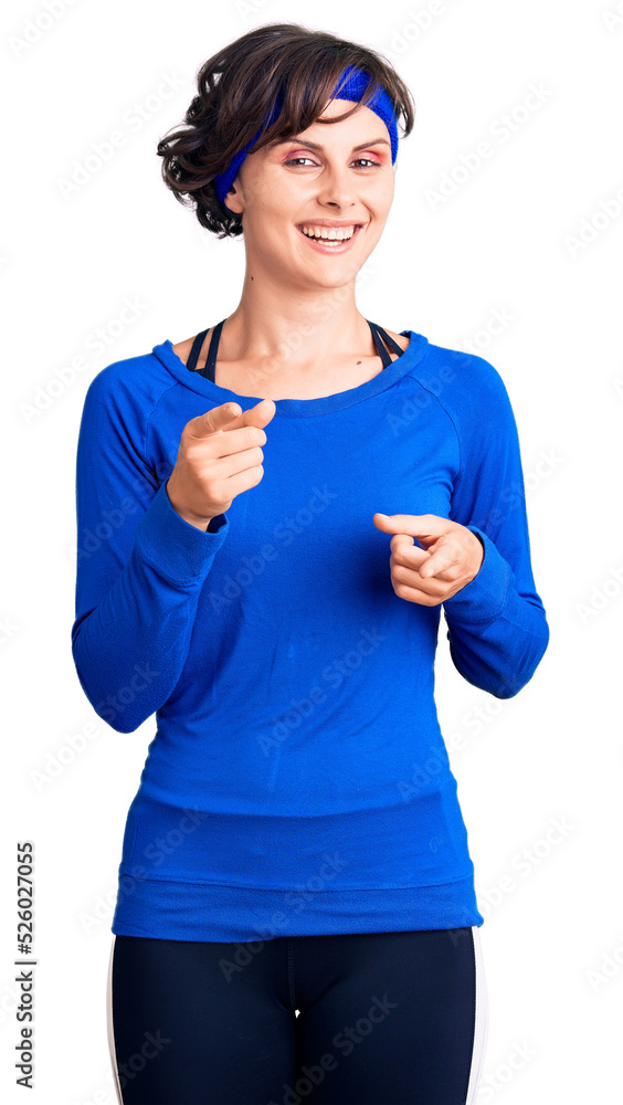 Beautiful young woman with short hair wearing training workout clothes pointing fingers to camera with happy and funny face. good energy and vibes. Beautiful young woman with short hair wearing training workout clothes pointing fingers to camera with happy and funny face. good energy and vibes.