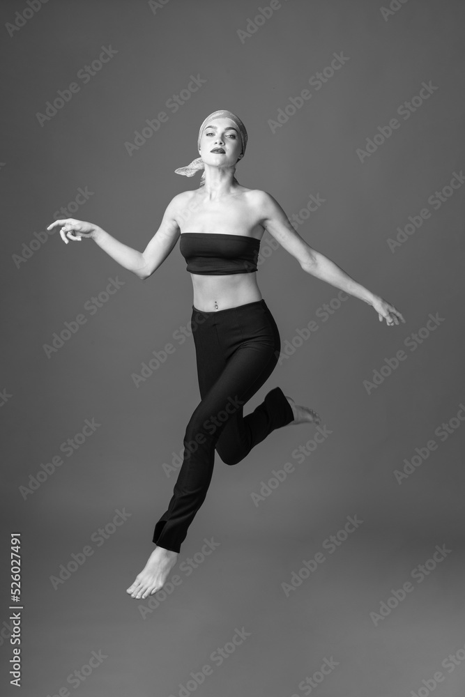 Sport, fashion and make-up concept. Slim and beautiful woman with black and tight sport outfit and scarf jumping in air. Graceful pose freeze in motion. Black and white image