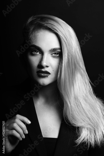 Fashion, make-up and business concept. Black and white studio portrait of beautiful woman with long bright hair looking at camera with seductive look. Model wearing classic black suit