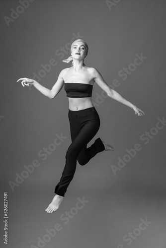 Sport, fashion and make-up concept. Slim and beautiful woman with black and tight sport outfit and scarf jumping in air. Graceful pose freeze in motion. Black and white image