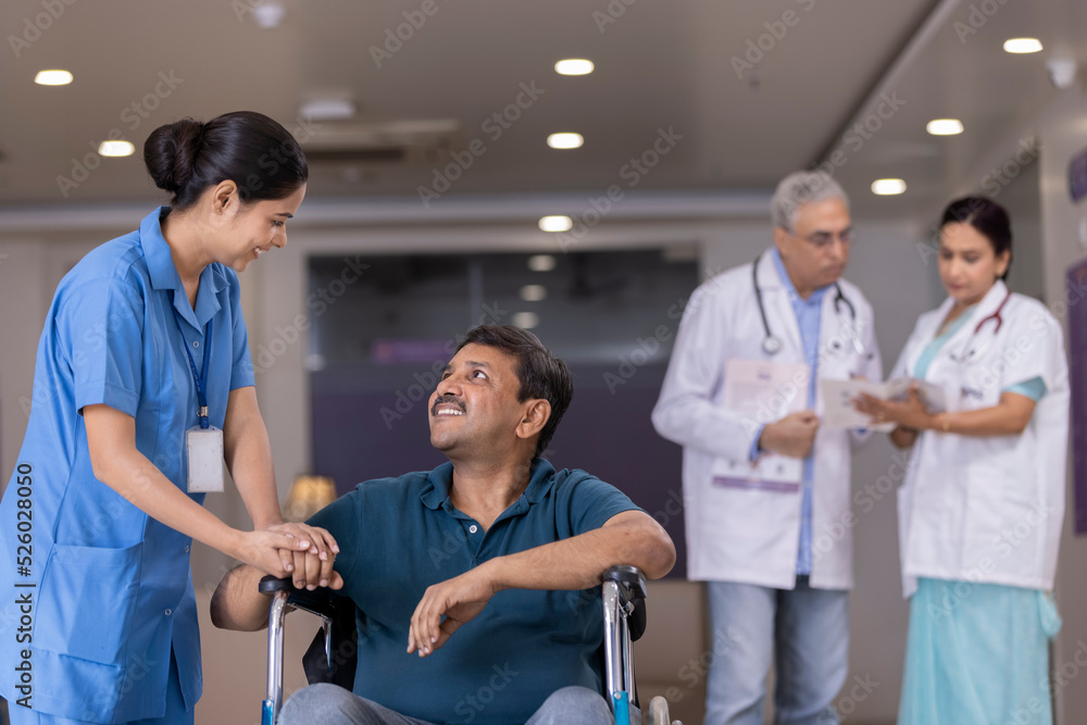 Obraz premium Nurse talking to disabled patient in wheelchair while doctors discussing in background at the hospital 