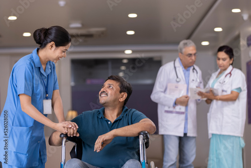 Nurse talking to disabled patient in wheelchair while doctors discussing in background at the hospital
