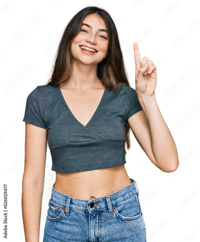 Young beautiful teen girl wearing casual crop top t shirt showing and pointing up with finger number one while smiling confident and happy. Young beautiful teen girl wearing casual crop top t shirt showing and pointing up with finger number one while smiling confident and happy.