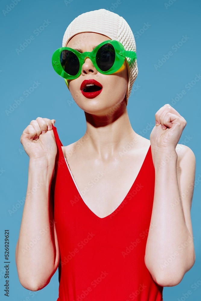 A surprised woman in a swimming cap opens her mouth holds the straps of a red swimsuit and looks away A surprised woman in a swimming cap opens her mouth holds the straps of a red swimsuit and looks away